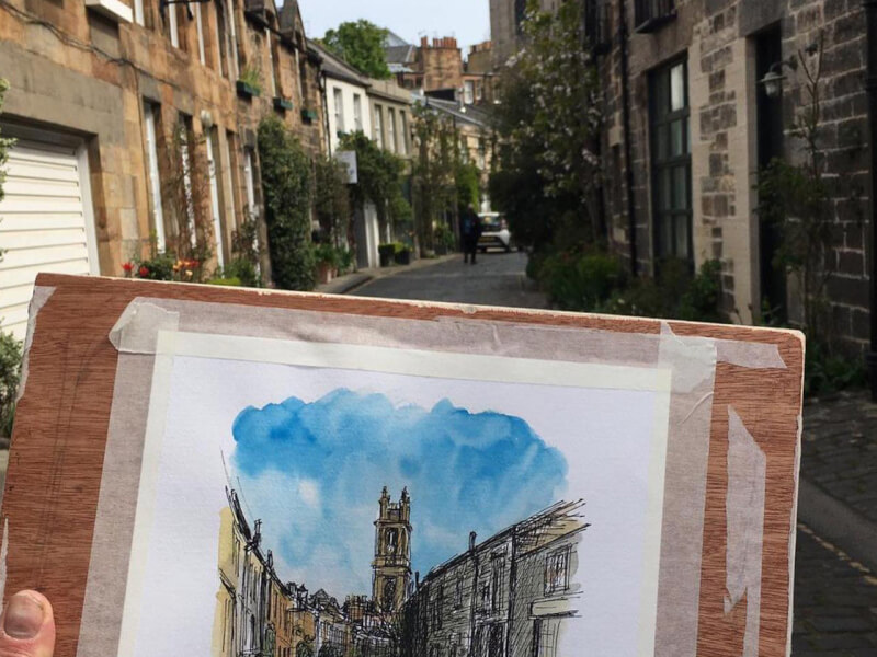 A sketchbook with a watercolour sketch positioned in front of the street that has been captured